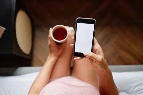 Overhead view of a woman using a smartphone while holding a coffee cup indoors.