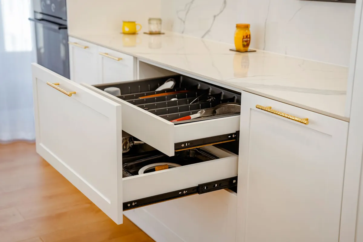 Elegant white kitchen drawer open with utensils, on marble counter.