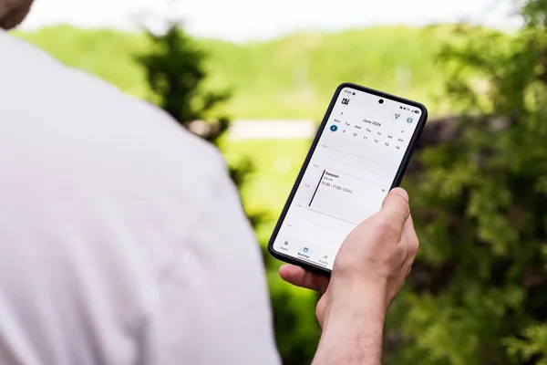 A person using a sauna booking app on a smartphone outdoors, surrounded by greenery.